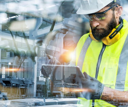Person nutzt ein Tablet zur Überwachung und Steuerung von Produktionsprozessen in einer modernen Fertigungsanlage.
