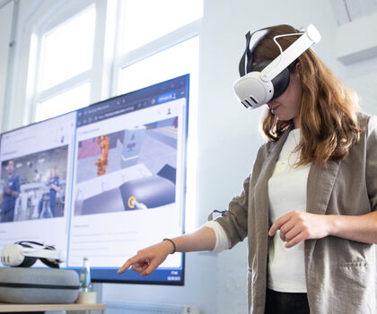 Person nutzt eine VR-Brille, um eine virtuelle Arbeits- und Produktionsumgebung zu erkunden.